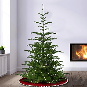 A sparse artificial Christmas tree with minimal branches and warm white lights, placed on a red tree skirt near a lit fireplace.