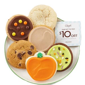 Assorted Cheryl's Halloween cookies are arranged on a plate, featuring a frosted pumpkin-shaped cookie, chocolate-frosted cookies, and a variety pack with a $10 off coupon.