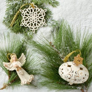 Three Christmas ornaments include a decorative snowflake, an angel with a \“2023\“ tag, and an ornate white and gold ornament, all set against snowy pine branches.