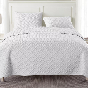 A white quilted bedspread with a textured geometric pattern covers a bed, accompanied by two matching pillows.