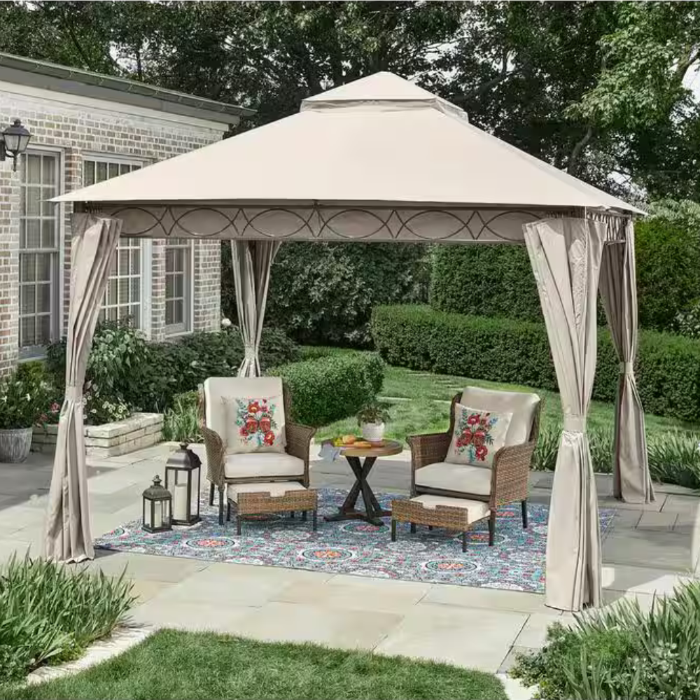 A patio with a beige canopy gazebo features two wicker armchairs with floral cushions, a small round table, and decorative lanterns on a patterned outdoor rug.