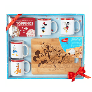 A gift set featuring four mugs with Disney characters, a wooden cutting board engraved with character images, a box of cocoa toppings, and a package for Mickey's hot cocoa bar.