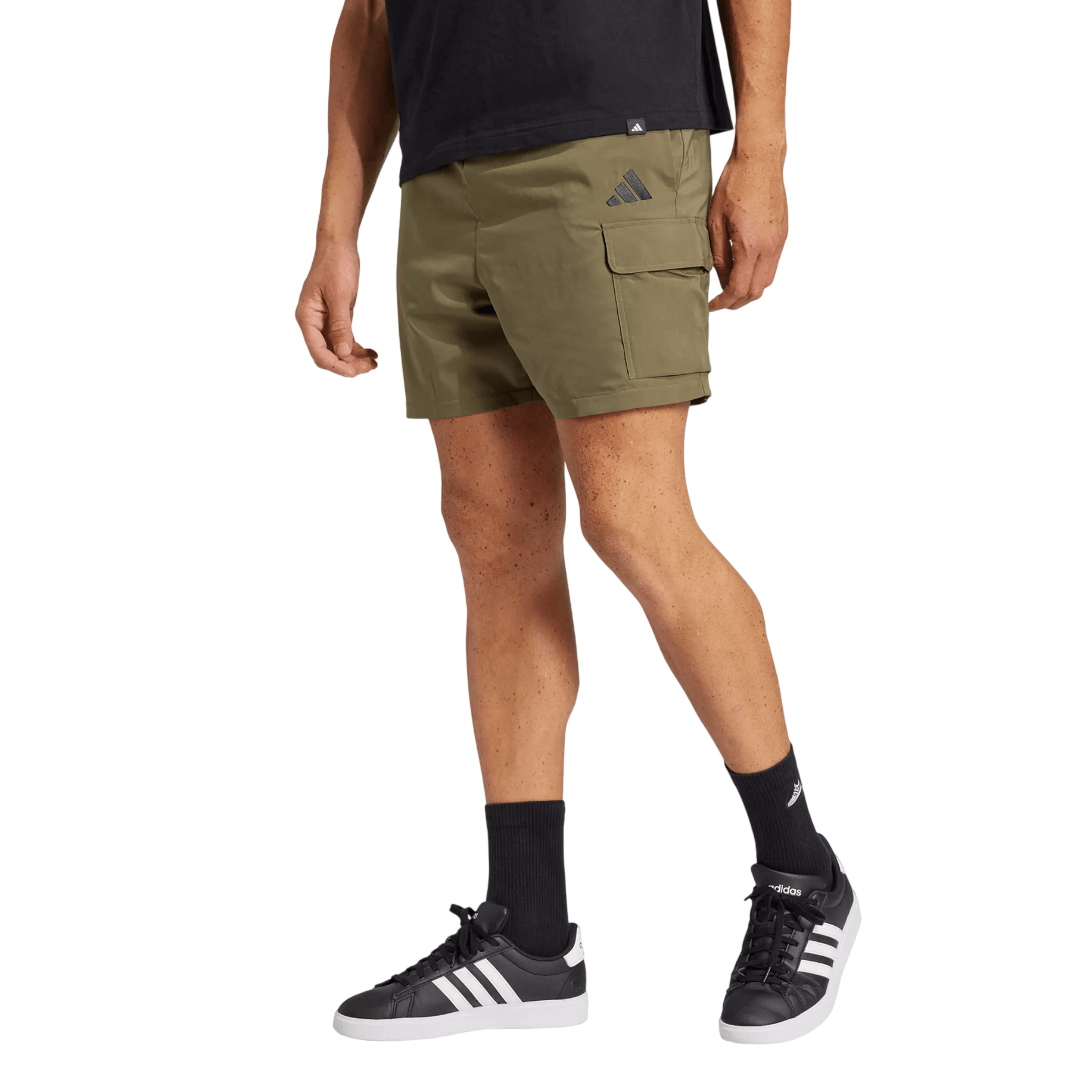 A person is wearing olive green cargo shorts with a logo on the left side, paired with black socks and black Adidas sneakers featuring white stripes.