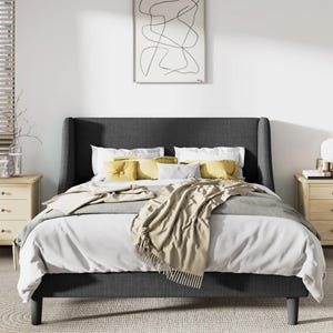 A modern bedroom setup with a dark upholstered bed, white and yellow bedding, a pair of wooden nightstands, and a wall art piece above the bed.