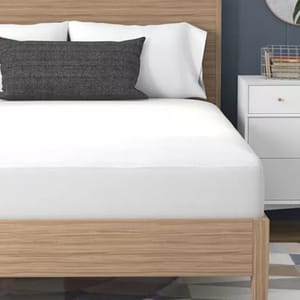 Wooden bed frame with a white mattress, two white pillows, a dark decorative pillow, and a white nightstand with books and a wired basket.