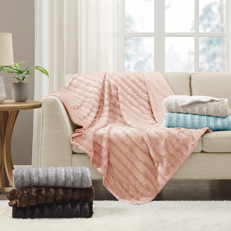 Assorted faux fur throw blankets in pink, blue, brown, and gray, draped over a sofa and folded on the floor.