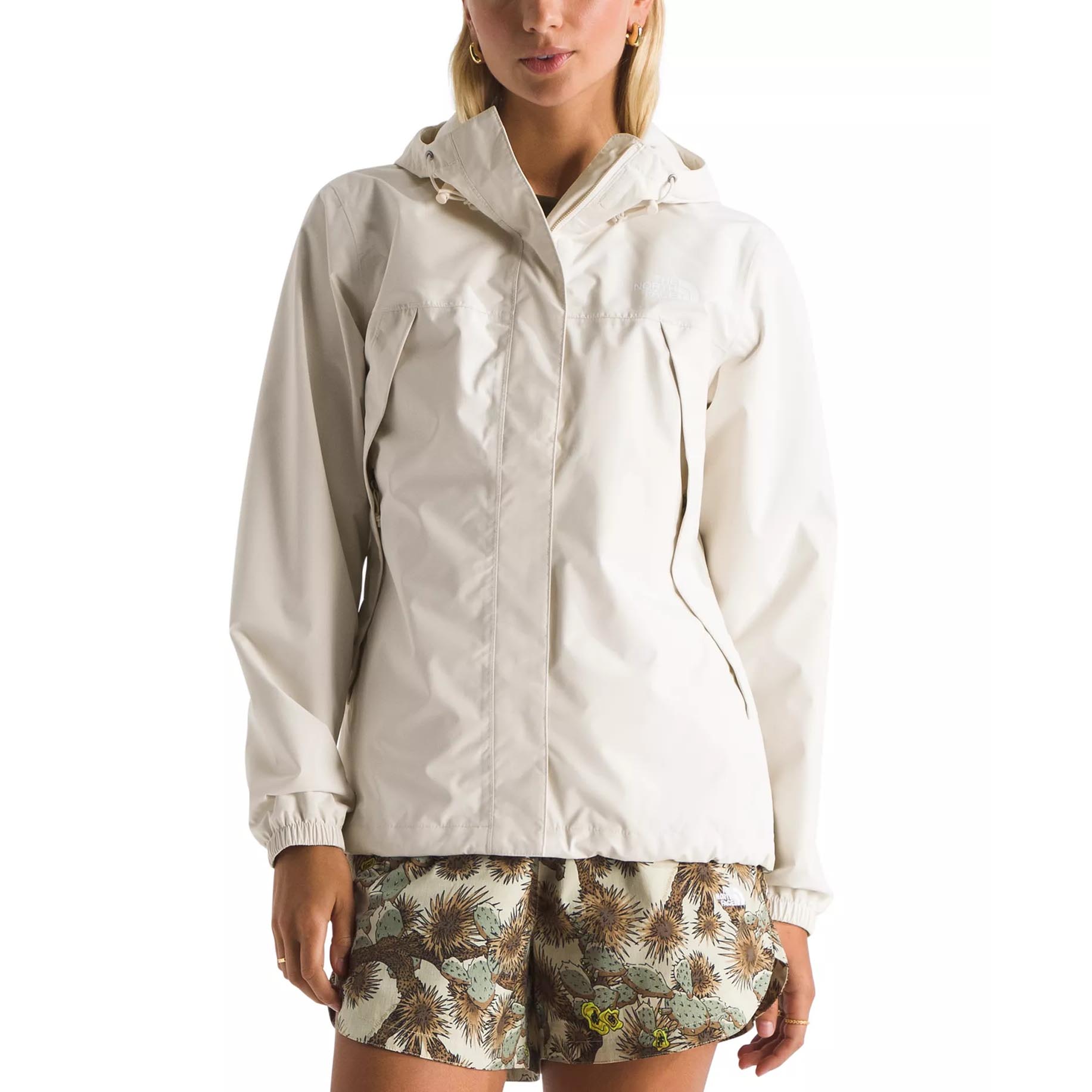 A person wearing an off-white waterproof jacket with a hood and elastic cuffs, paired with patterned shorts featuring a desert plant design.