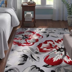 A floral patterned area rug with large red and gray flowers on a light background, positioned in a room with furniture.