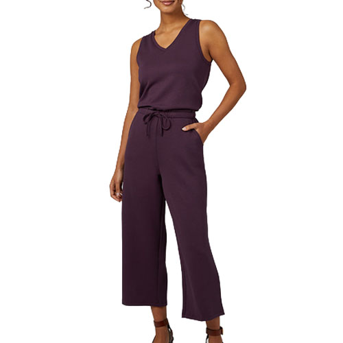 Sleeveless dark purple jumpsuit with a V-neck, wide-leg cropped pants, and a waist tie, styled with heeled sandals.