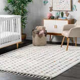 A nursery features a white crib, a textured rug with colorful dots, a basket with plush toys, a sideboard with decorations, a tall plant, and a beige armchair. Walls are adorned with a playful dot painting and wall-mounted animal figures.