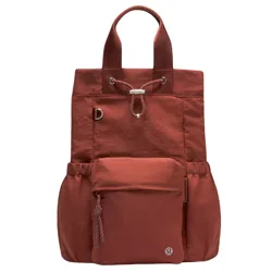 A rust-colored tote backpack with short handles, a front pocket, drawstring closure, and side pockets. It features a small circular logo at the front.