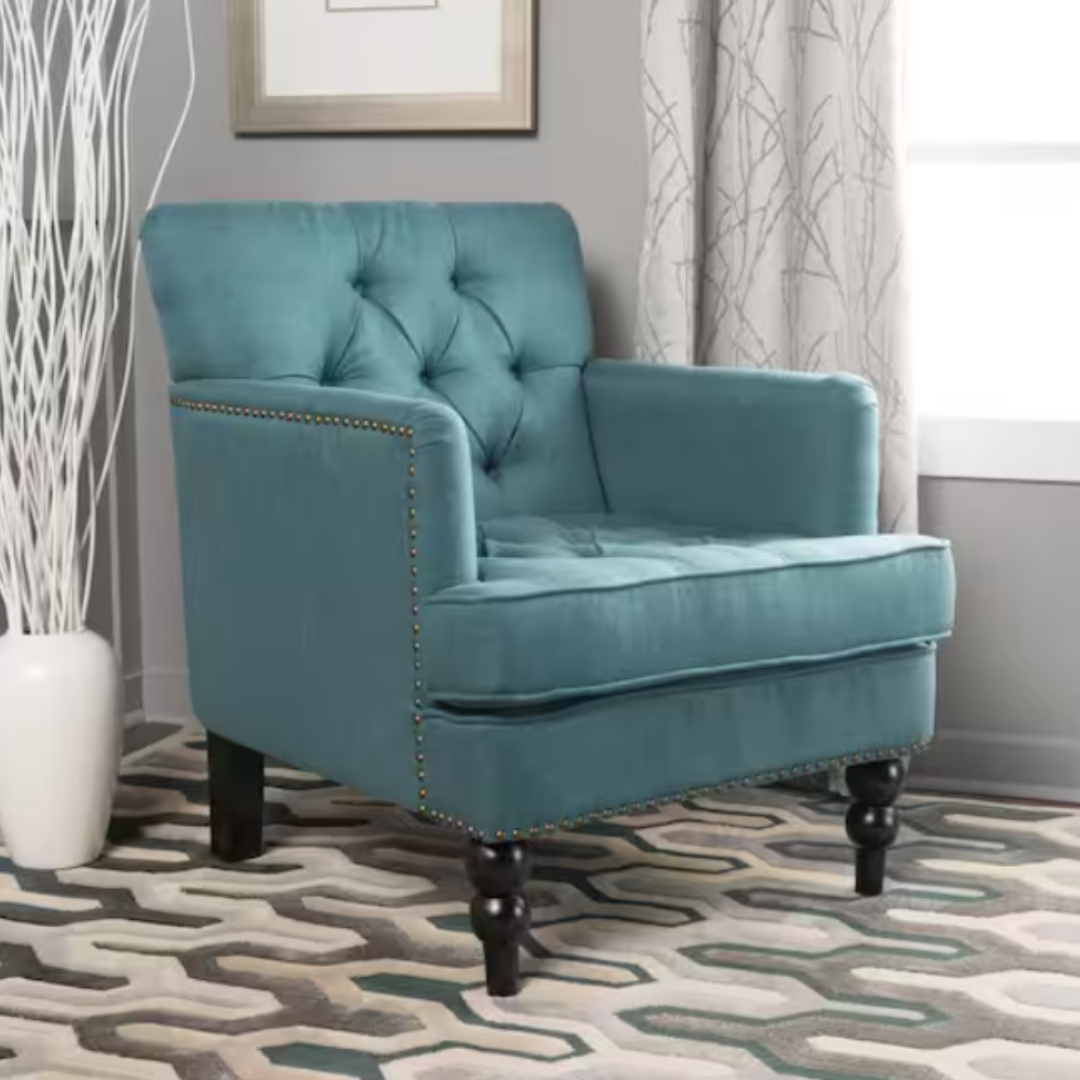 A teal upholstered armchair with tufted back, nailhead trim, and dark wooden legs, on a geometric patterned rug.