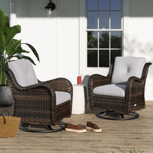 Two wicker swivel chairs with grey cushions on a patio, alongside a white side table and a pair of women’s shoes.