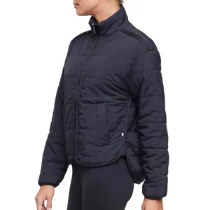 A person is wearing a black, quilted puffer jacket with a high collar and side pockets. The jacket has a slightly cropped design, paired with black leggings.