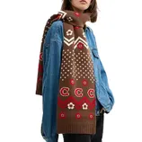 A person is wearing a denim jacket paired with a cozy, brown knit scarf featuring a geometric and floral pattern in red and cream.