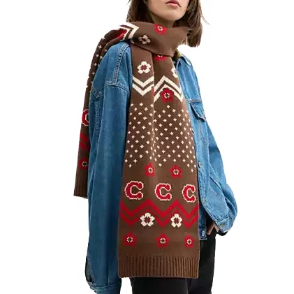A person is wearing a denim jacket paired with a cozy, brown knit scarf featuring a geometric and floral pattern in red and cream.