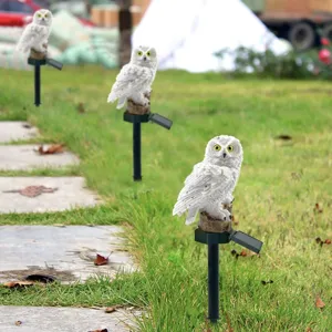 The photo shows three owl-shaped garden lights with solar panels mounted on stakes, placed along a stone pathway in a grassy area.