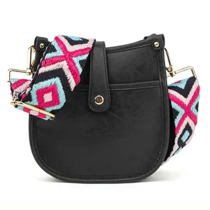 A black shoulder bag with a colorful, geometric-patterned strap featuring shades of pink, blue, and black, accented with gold-tone hardware.