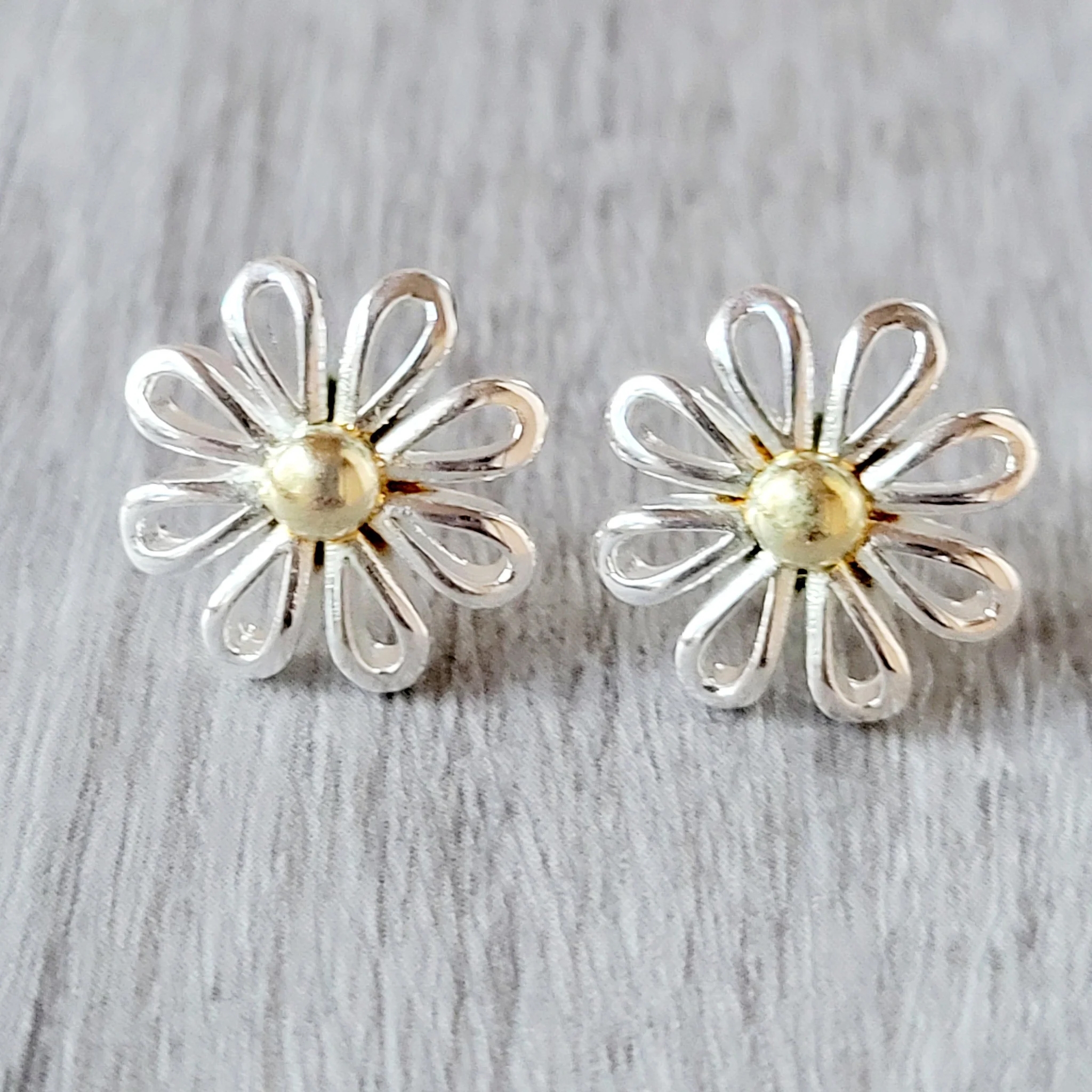 Pair of flower-shaped earrings with silver petals and a gold center, set on a textured gray surface.