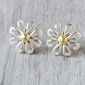 Pair of flower-shaped earrings with silver petals and a gold center, set on a textured gray surface.
