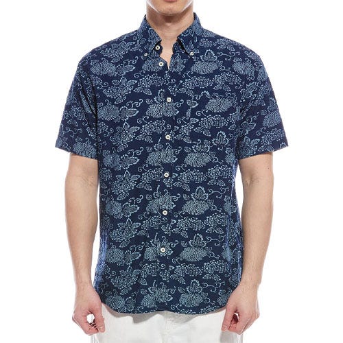 A short-sleeve button-up shirt with a navy blue background and light blue floral pattern, worn by a person with white pants.