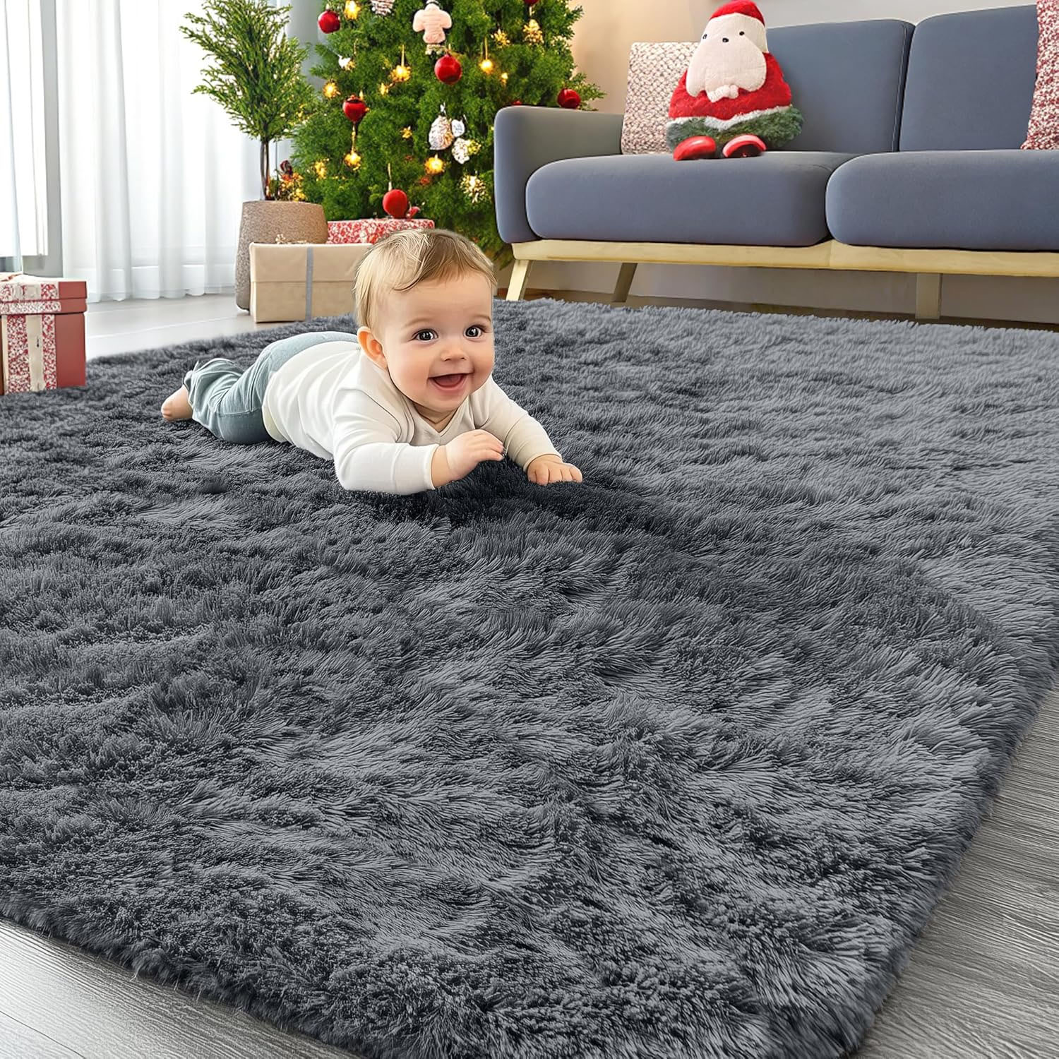A gray, 4' x 6' shag rug is on the floor in a living room with a baby playfully lying on it, and there's a Christmas-themed setup with a tree, presents, and Santa decoration nearby.