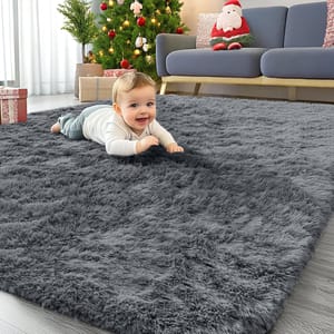 A gray, 4' x 6' shag rug is on the floor in a living room with a baby playfully lying on it, and there's a Christmas-themed setup with a tree, presents, and Santa decoration nearby.