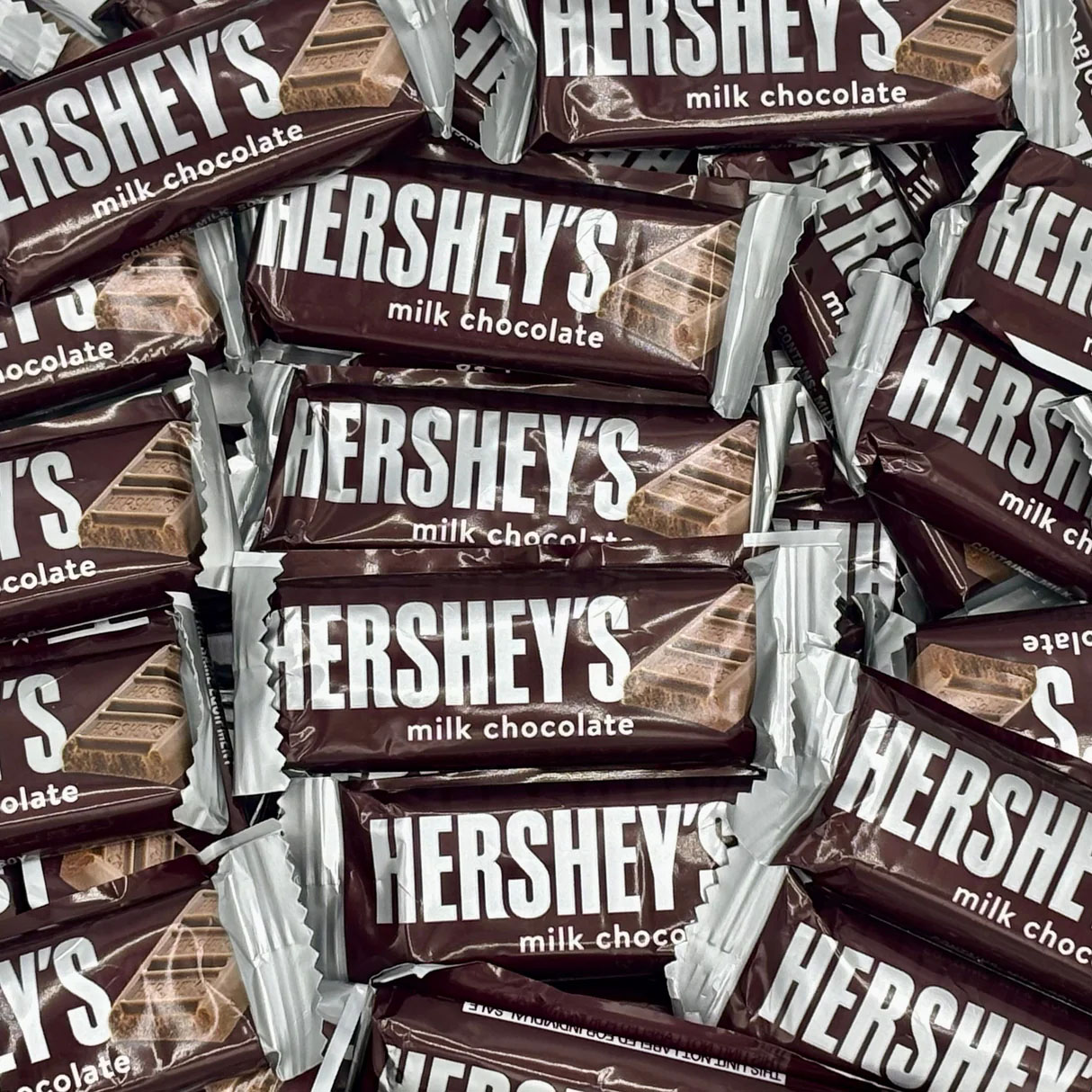 A pile of snack-sized Hershey's milk chocolate bars with brown and white packaging, featuring the Hershey's logo prominently displayed.