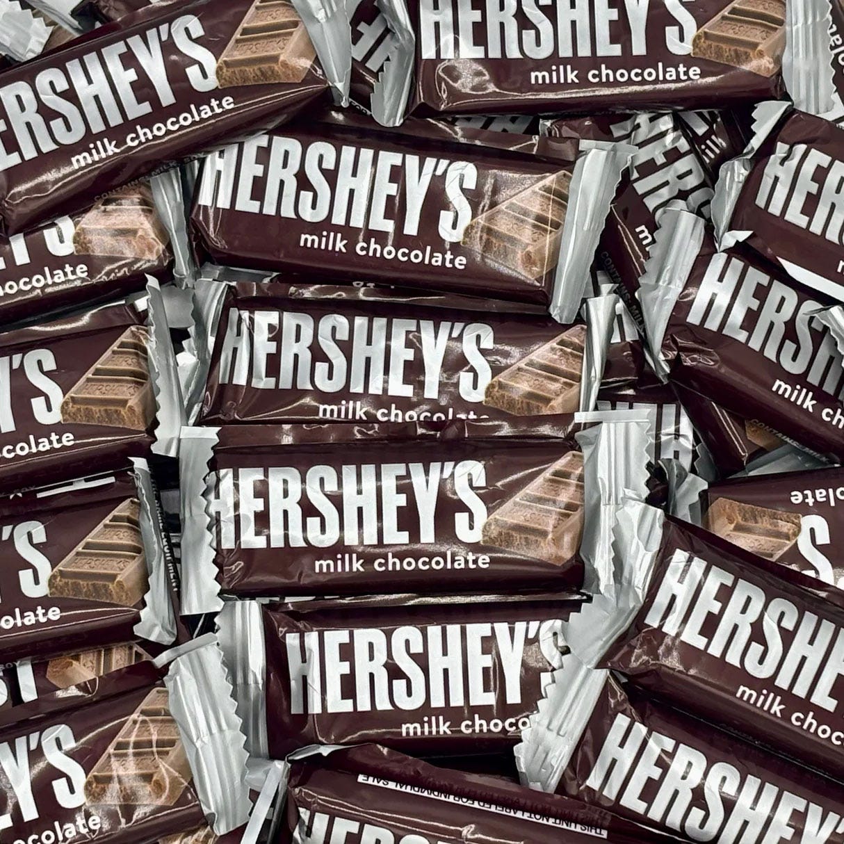 A pile of snack-sized Hershey's milk chocolate bars with brown and white packaging, featuring the Hershey's logo prominently displayed.