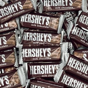A pile of snack-sized Hershey's milk chocolate bars with brown and white packaging, featuring the Hershey's logo prominently displayed.
