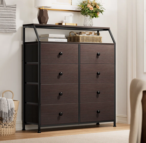 A dark brown dresser with eight drawers featuring black knobs stands on a wooden floor. It has a metal frame, and is topped with a shelf displaying a lamp, books, a basket, and flowers in a vase.