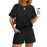 A person is wearing a black short-sleeve top and matching shorts with a drawstring waist, holding a cup and a black shoulder bag.