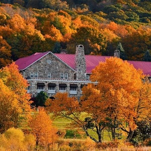 Stone house with a red roof surrounded by trees with autumn foliage.