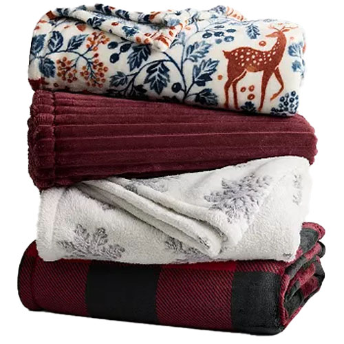 A stack of four cozy blankets featuring various designs: a floral-and-deer pattern, a solid burgundy, a snowflake print, and a red-and-black checkered pattern.