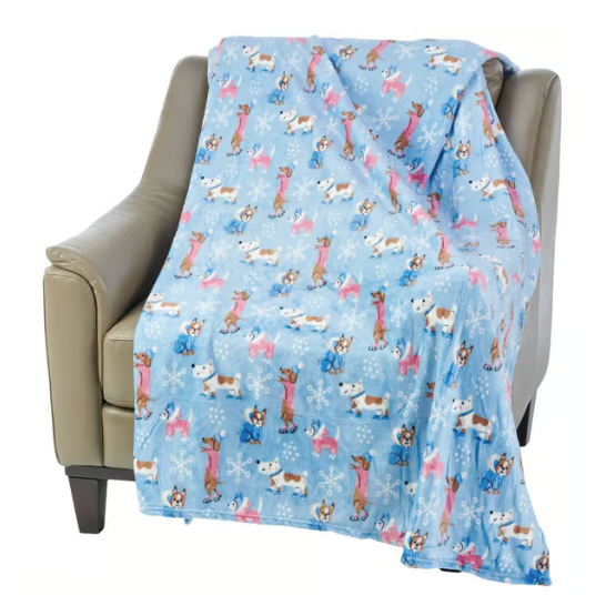 A light blue fleece blanket with a pattern of cartoon dogs and snowflakes is draped over a beige armchair.