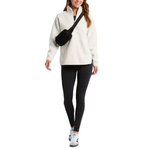 A white faux-shearling pullover with a quarter-zip neck and long sleeves, styled with black leggings, a crossbody bag, and sneakers.