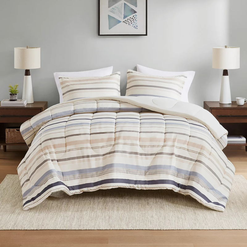 A bedroom setting features a bed with a striped comforter and matching pillowcases, flanked by two wooden nightstands with lamps. A small plant and a framed geometric artwork add decor elements.