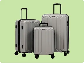 A set of three silver hard-shell suitcases with black handles and wheels, displayed against a light green background.