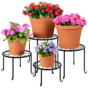 Four black metal plant stands of varying heights with round tops, each holding a terracotta pot with colorful flowers.