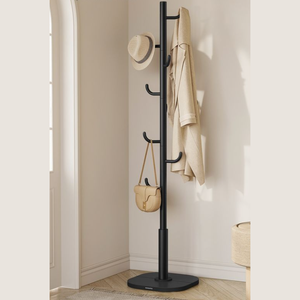 A black coat rack stands in the corner with six hooks, holding a tan hat, coat, and handbag against a light-colored wall.