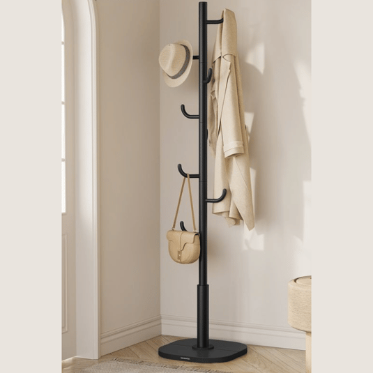 A black coat rack stands in the corner with six hooks, holding a tan hat, coat, and handbag against a light-colored wall.