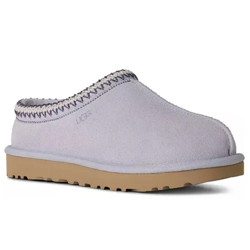 A lavender-colored suede clog slipper with visible stitching, a tan rubber sole, and a small \“UGG\“ logo on the side.