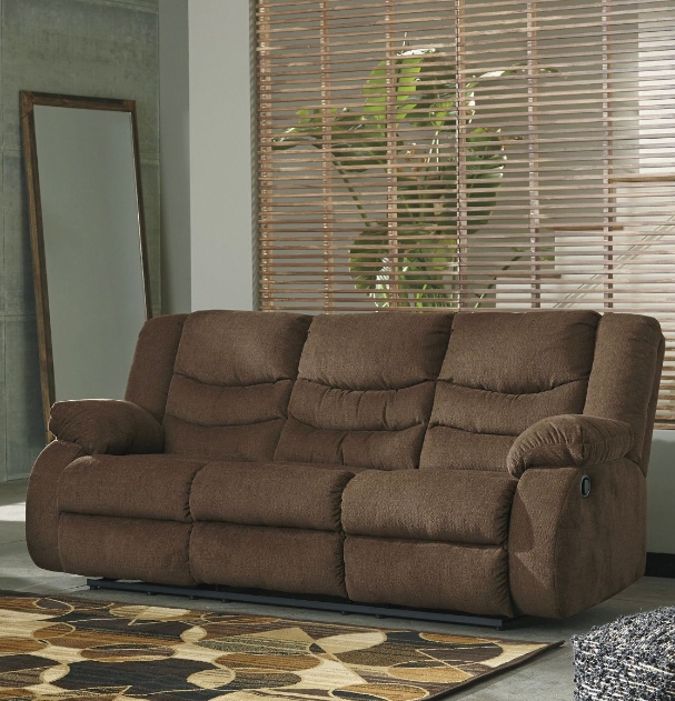 Brown reclining sofa with plush cushions in a room with blinds and a patterned area rug.