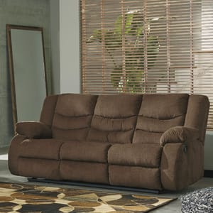 Brown reclining sofa with plush cushions in a room with blinds and a patterned area rug.