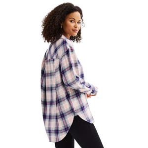 A woman is wearing a long-sleeved, oversized plaid shirt with shades of pink, purple, and blue, paired with black pants.