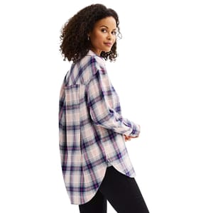 A woman is wearing a long-sleeved, oversized plaid shirt with shades of pink, purple, and blue, paired with black pants.