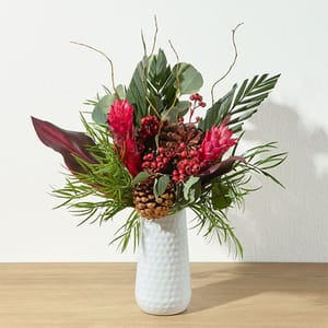 A vibrant floral arrangement in a white textured vase features pink flowers, pinecones, and assorted greenery with a natural, organic look.