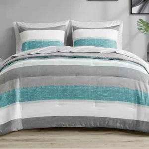 A bed is adorned with striped bedding in shades of gray, white, and teal. Matching pillows complement the comforter with similar patterns.