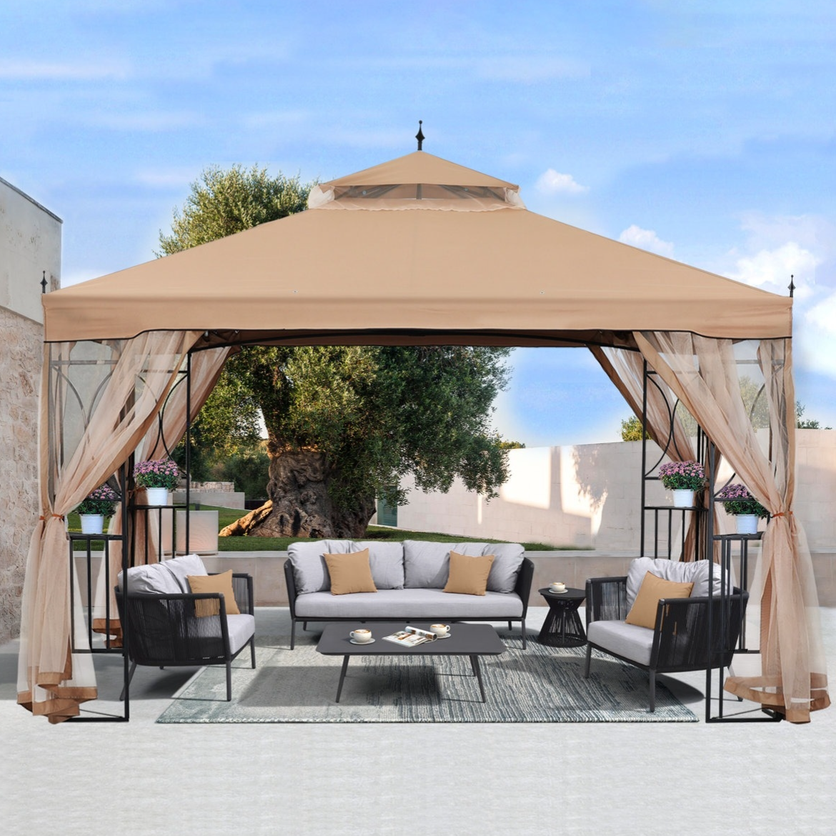 Outdoor gazebo with a beige canopy, featuring a patio furniture set including a sofa, two chairs, and a coffee table. The setup is accessorized with cushions and potted plants, situated on a rug against a backdrop of trees and a stone wall.