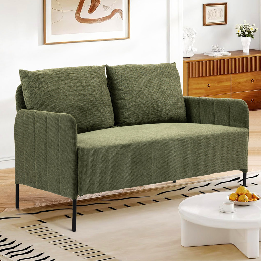 Green chenille upholstered loveseat with two cushions, quilted armrests, and slim black metal legs. It is set in a living room with a light wood console, decorative art, and a beige rug featuring black line designs.